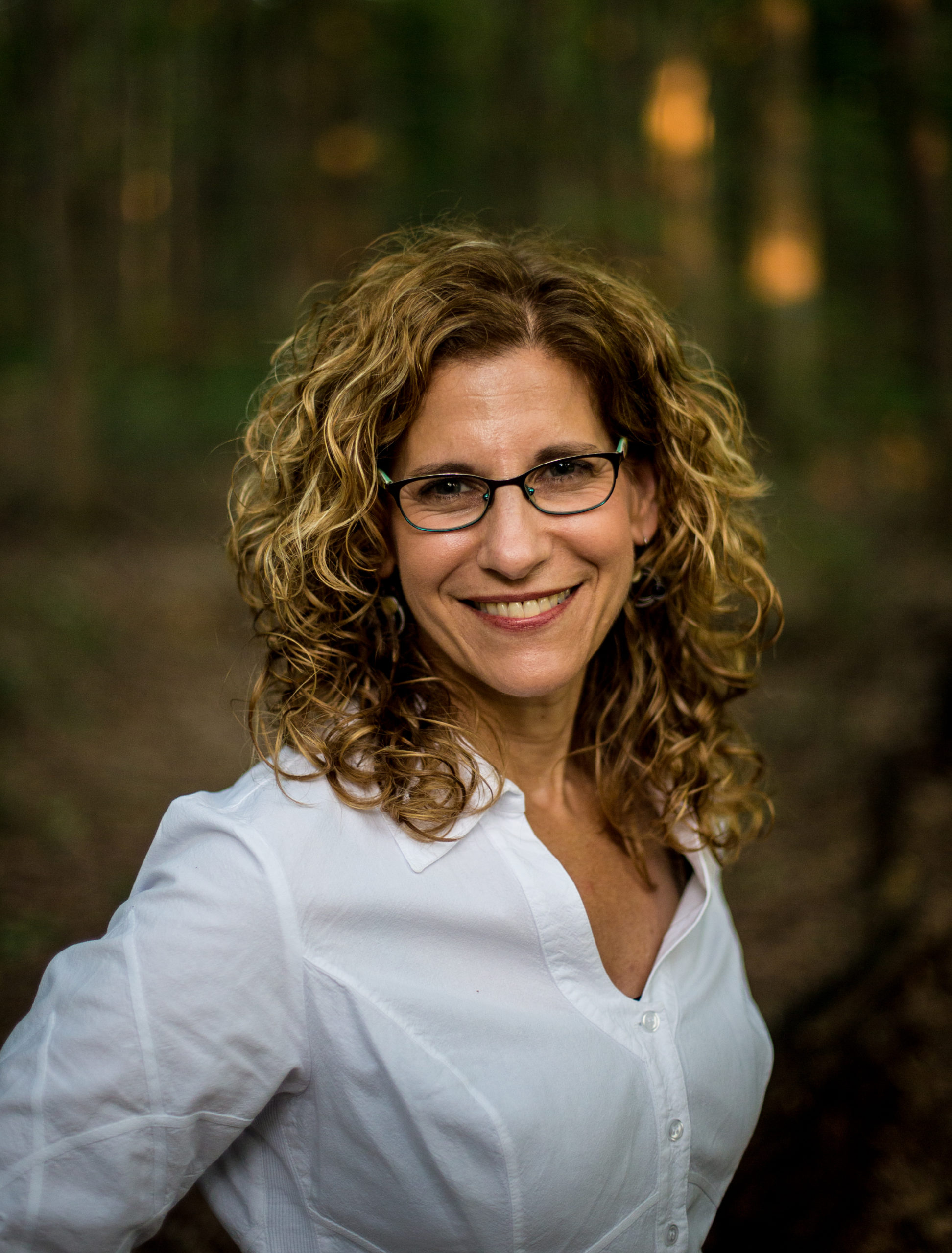 professional headshot of woman with curly hair and glasses smiling at the camera